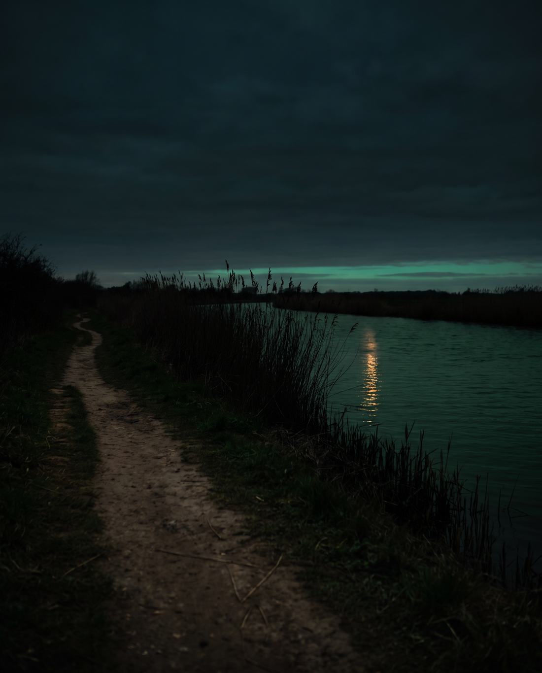 A narrow footpath along a riverbank at dusk